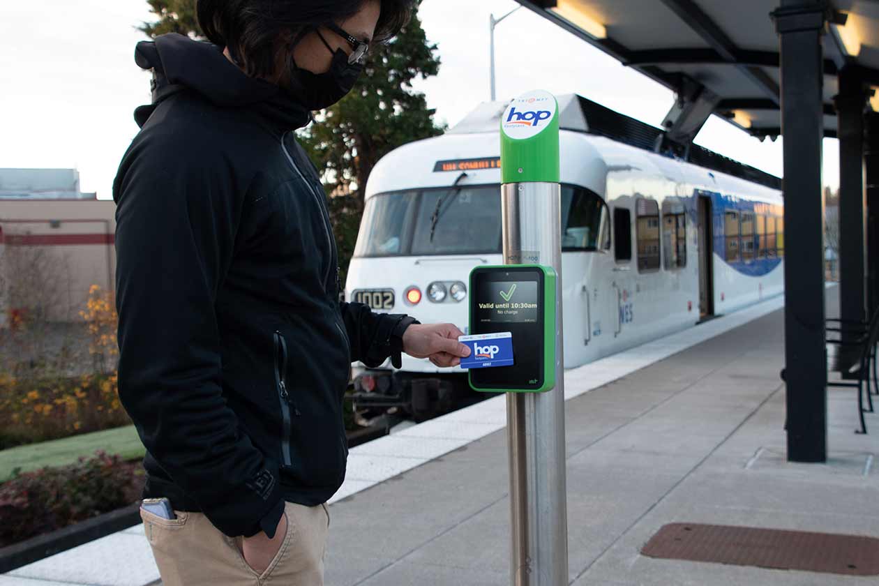 Rider tapping Hop reader on WES platform, with composition that shows both the location of Hop reader and appearance of Hop reader enough to see welcome screen with Hop logo and where to tap.